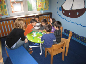 Erzieherin und Kinder sitzen um Tisch.