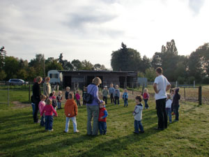 Kinder und Erwachsene stehen im Kreis auf Pferdewiese.