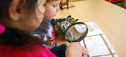 Zwei Kinder lesen ein Buch mit Lupe