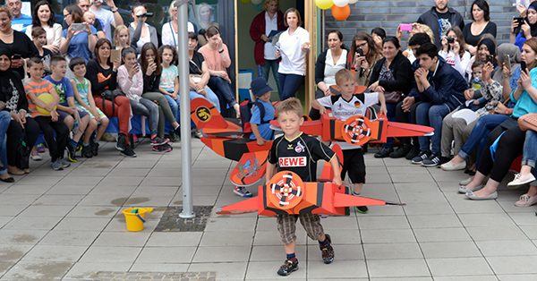 Kinder tragen große selbstgebastelte Flugzeuge um den Bauch