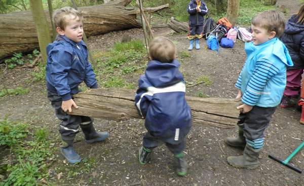 3 Jungen tragen einen Baumstamm.