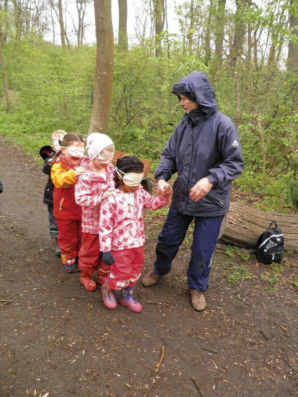 Erzieherin und Kinder in Kette mit verbundenen Augen im Wald.