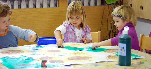 3 Kinder malen am Tisch auf ein großes Papier