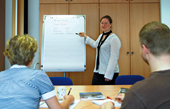 Frau neben Flipchart vor zwei sitzenden Schülern