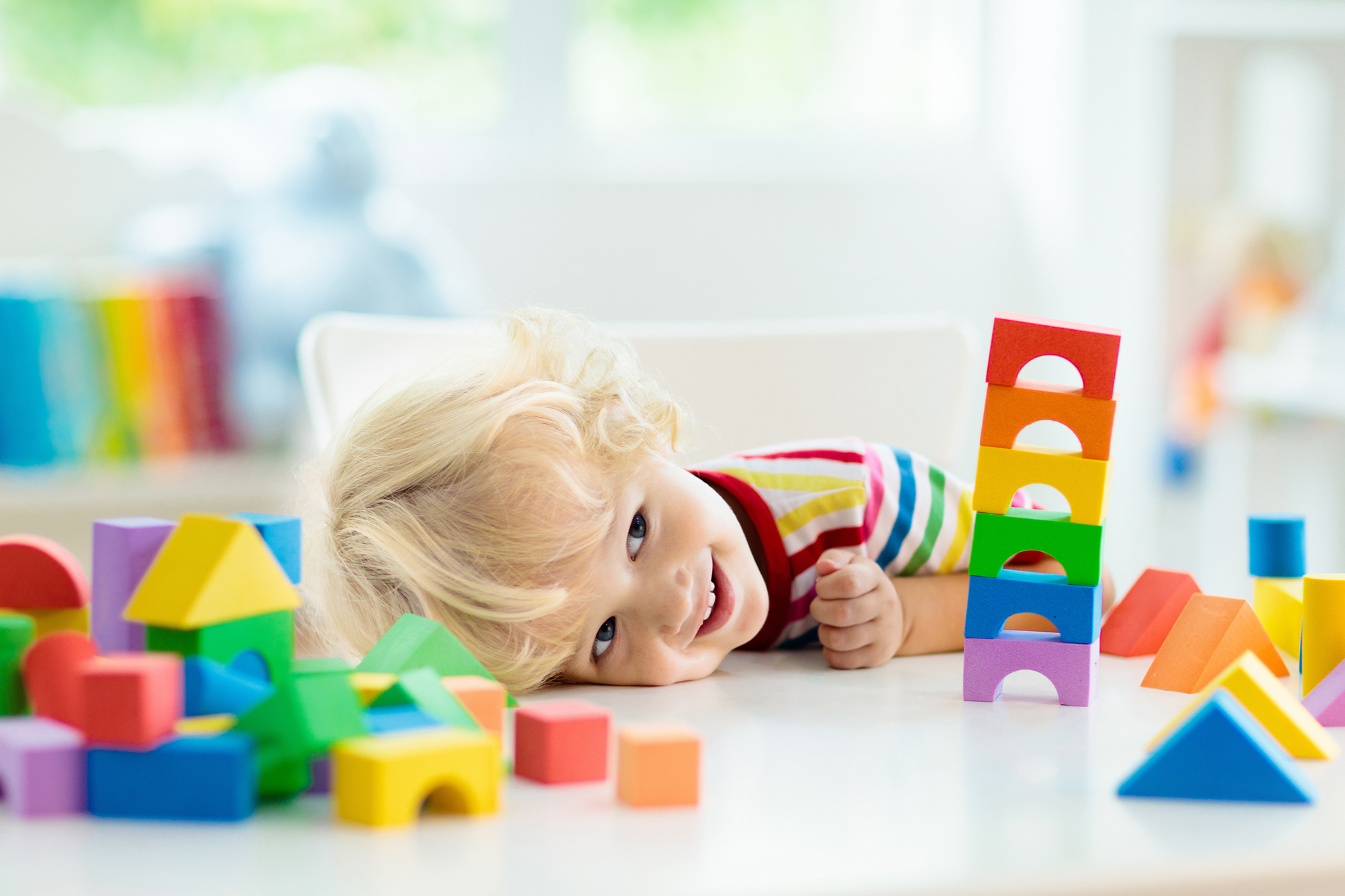 Kinderkopf liegt auf einem Tisch und schaut sich bunte Spielklötze an